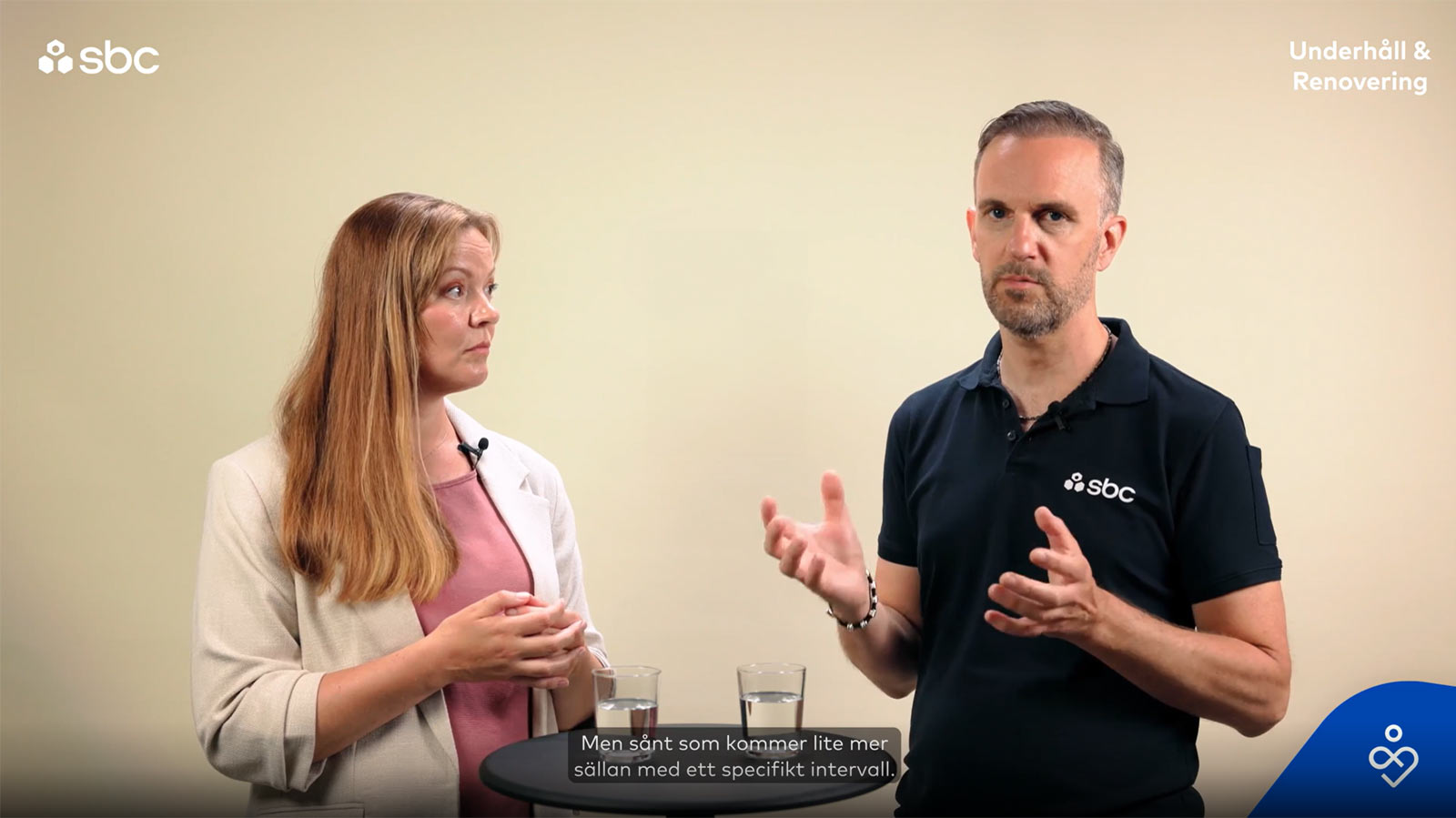 En man och en kvinna står i en studio och samtalar om vikten av en underhållsplan för Brf:er.