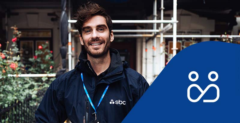 SBCs byggprojektledare Patrik står framför en fastighet med byggnadsställning och rosenrabatt. Projektledningsikon.