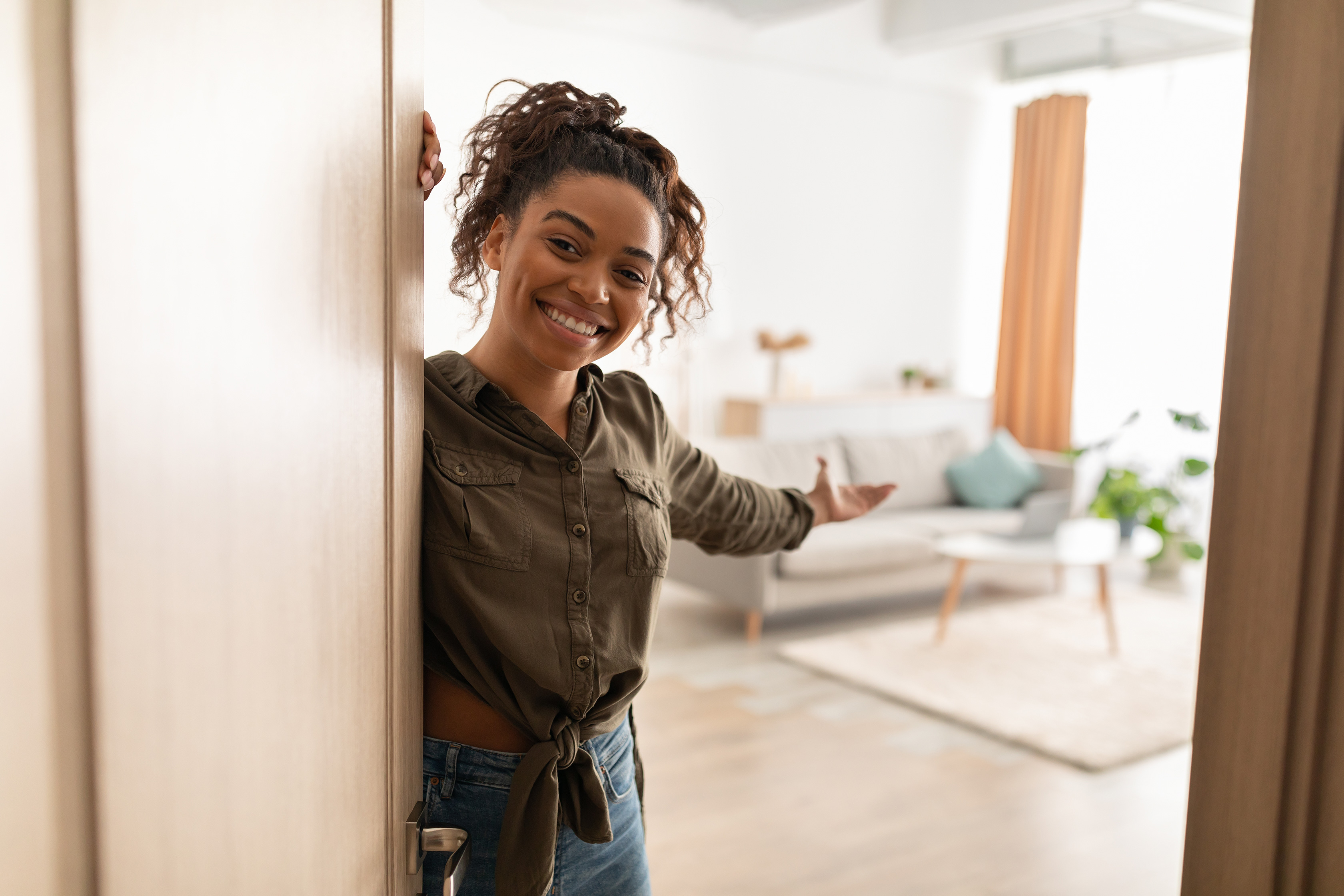 Kvinna öppnar sin ytterdörr och gör en välkomnande gest