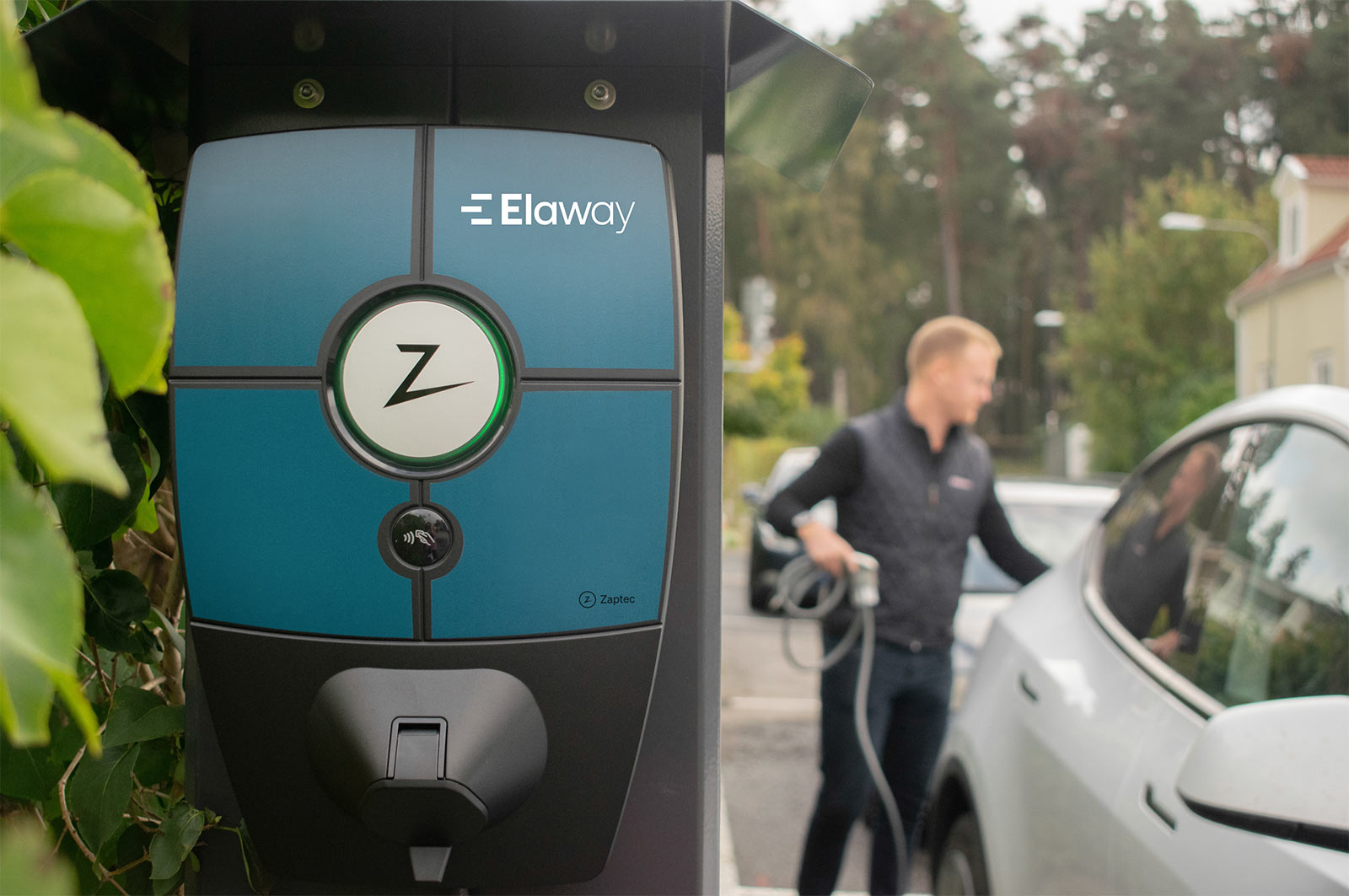 Elbilsladdare från Elaway i förgrunden och man som laddar sin bil i bakgrunden.