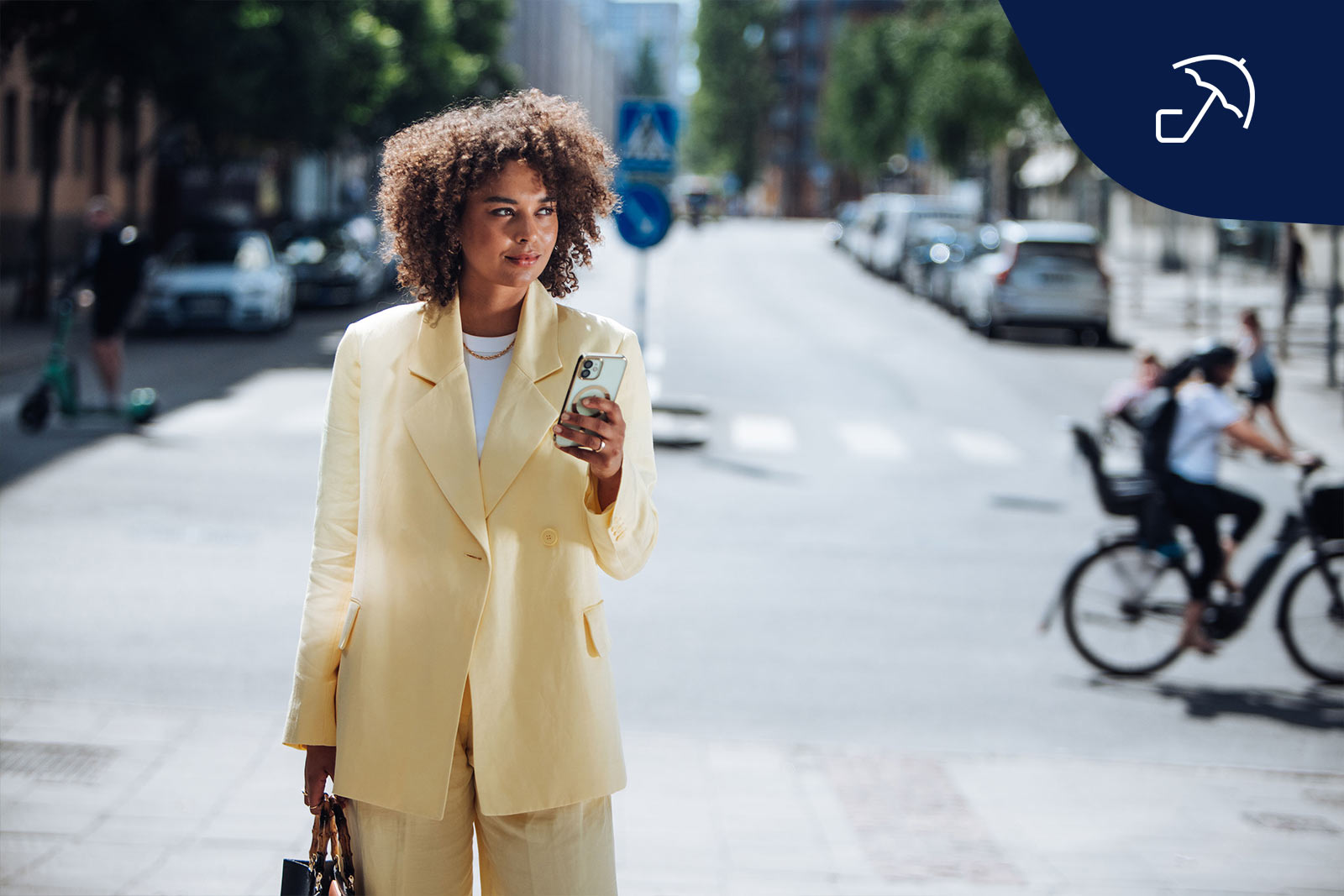 Kvinna i gul kostym står på gatan med mobiltelefon i handen.