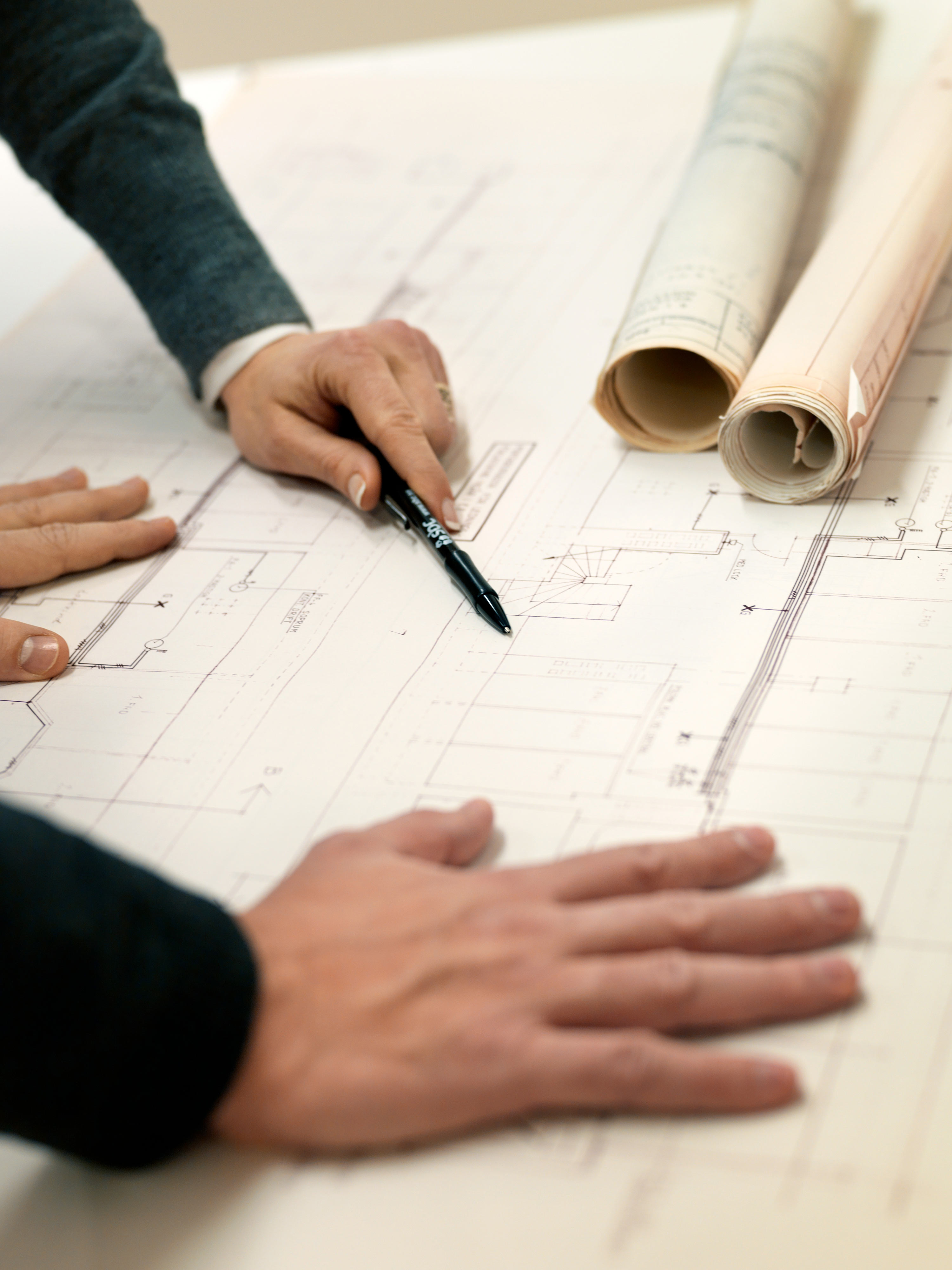 Två par händer granskar byggnadsritningar som ligger på ett bord