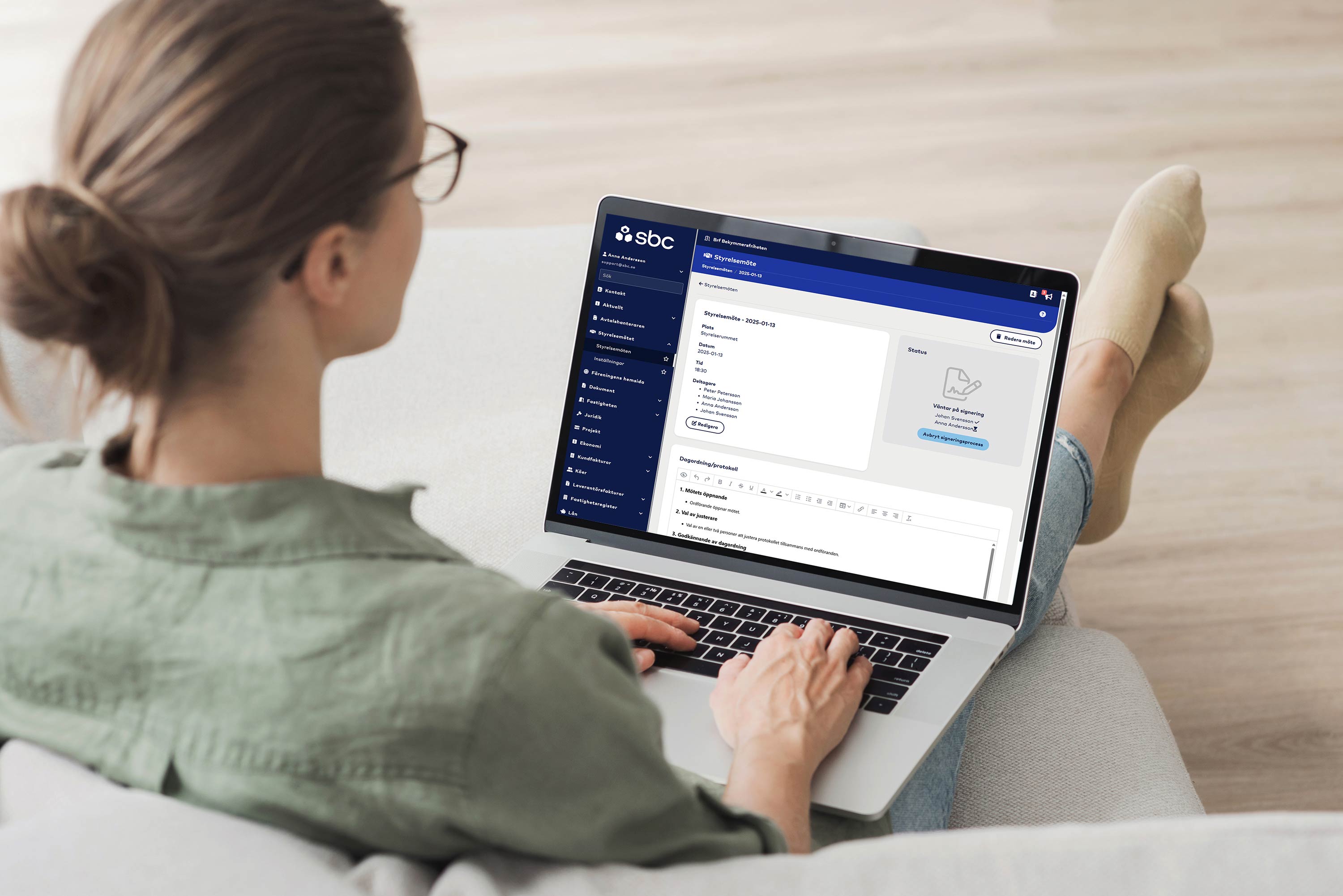 Kvinna sitter i soffan med en laptop i knät och besöker SBC Hemma och sidan för styrelsemötet.