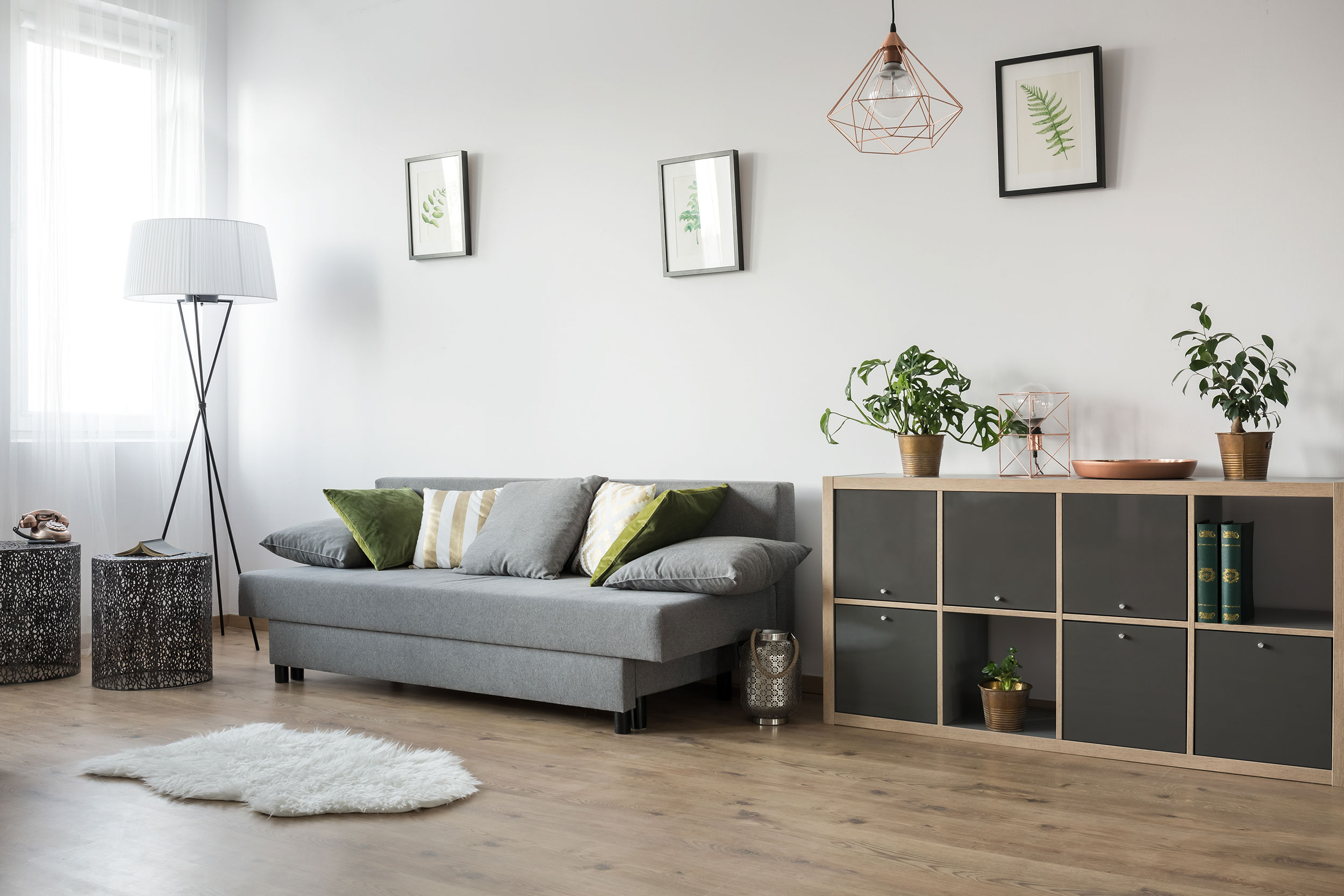 Hyresrätt möblerad med grå soffa, låg bokhylla och golvlampa