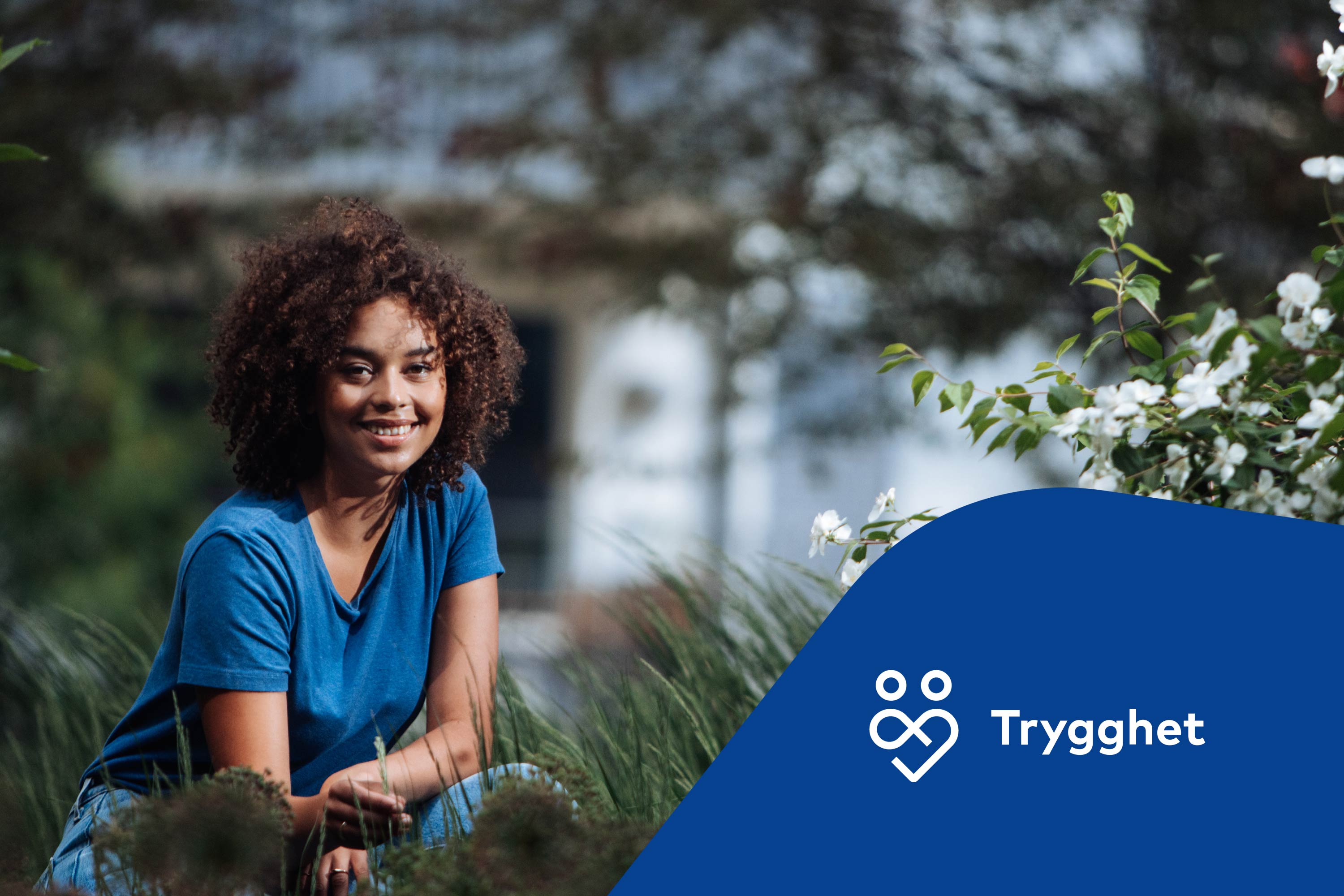 Kvinna sitter på huk i gräset med en fastighet i bakgrunden. Trygghetsikon.